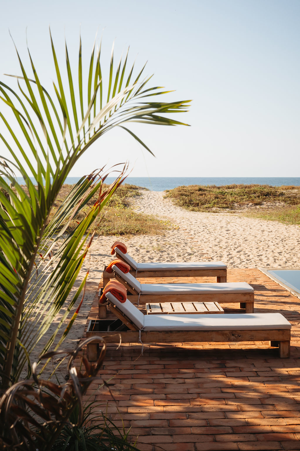 Wooden lounge chairs on a brick patio facing the beach at Casa Arena in Mexico