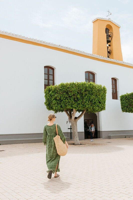 Woman walking toward a white building with a bell tower and trimmed trees