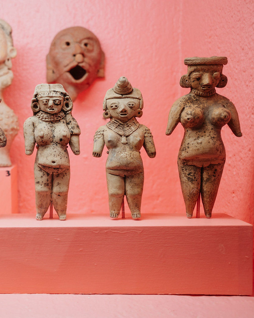 Ancient Mesoamerican clay figurines displayed against a pink background wall in Mexico