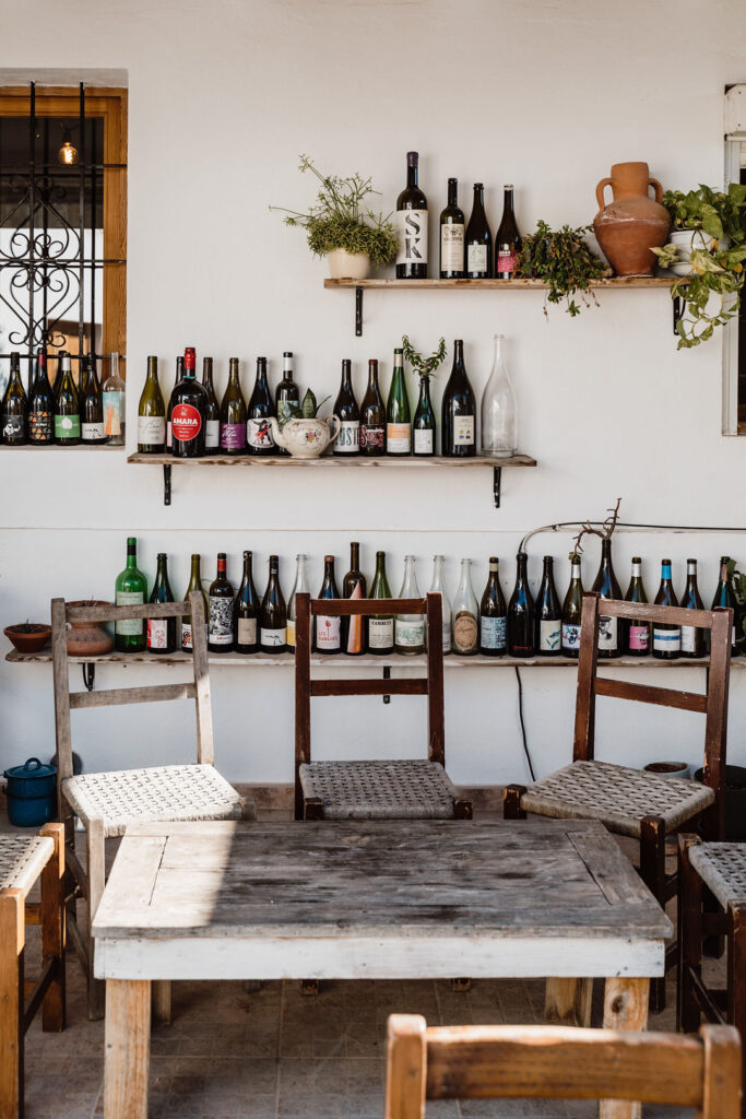 Wine bottles line shelves above a rustic table and woven-seat chairs at a countryside gathering spot near Can Romero Villa in Santa Eulalia, Ibiza.