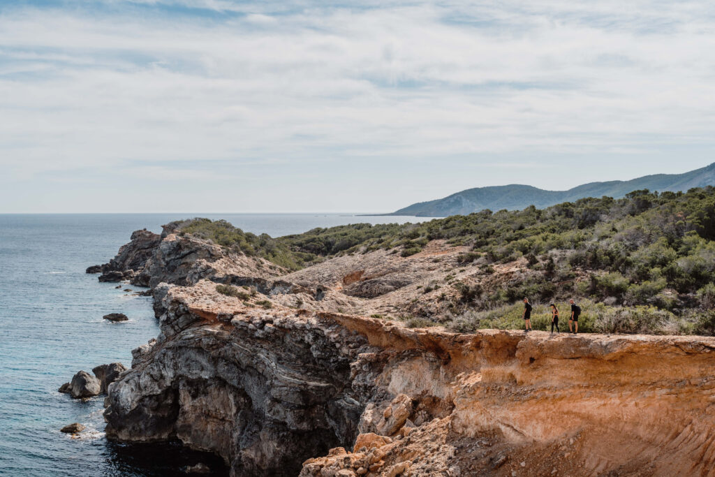 Hikers follow a rocky coastal trail above the sea near Can Romero Villa in Santa Eulalia, Ibiza.