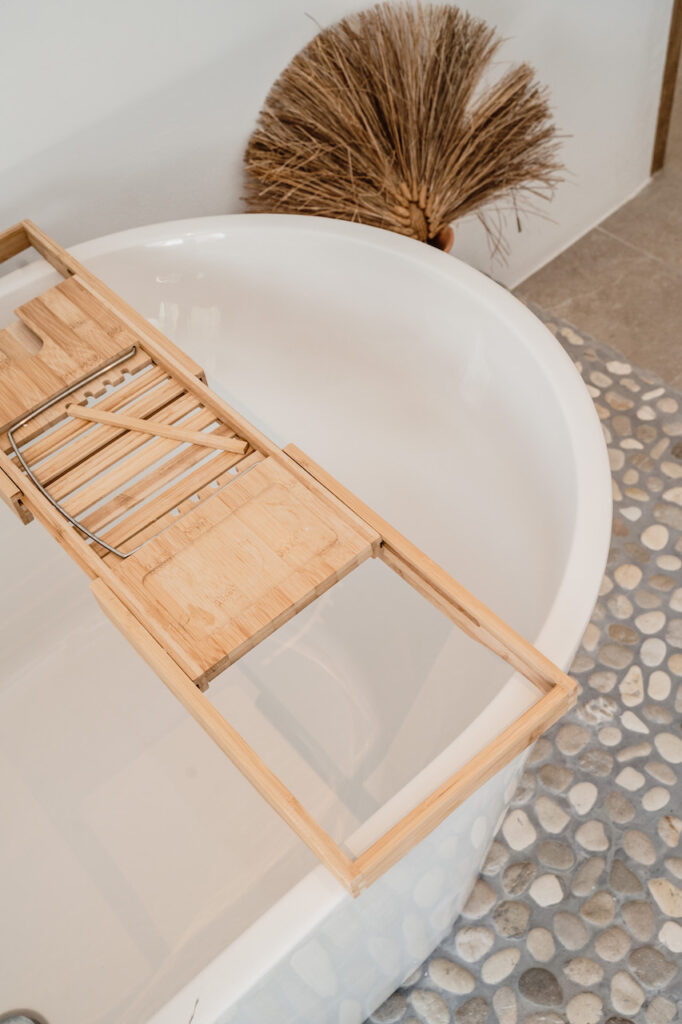 A freestanding white bathtub has a wooden bath caddy and pebble-tile surround at Can Romero Villa in Santa Eulalia, Ibiza.
