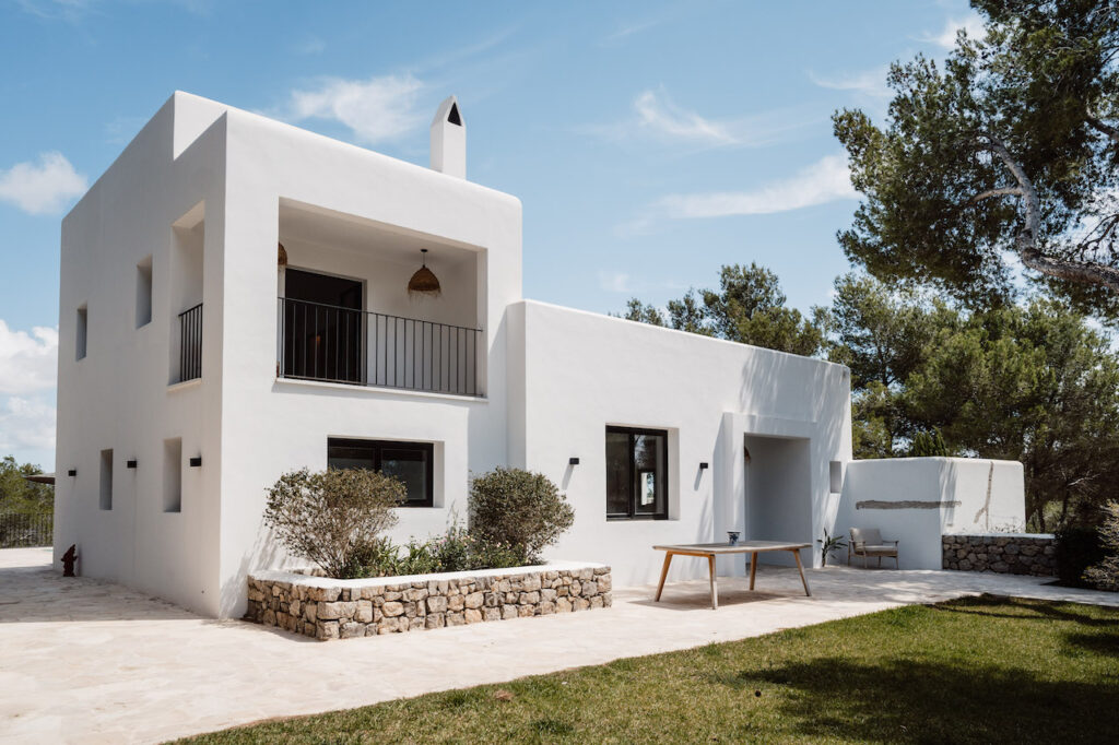 The villa’s white exterior opens onto a stone patio and green lawn at Can Romero Villa in Santa Eulalia, Ibiza.