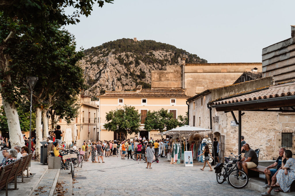 Busy Mallorca village square with market stalls and mountain views.
