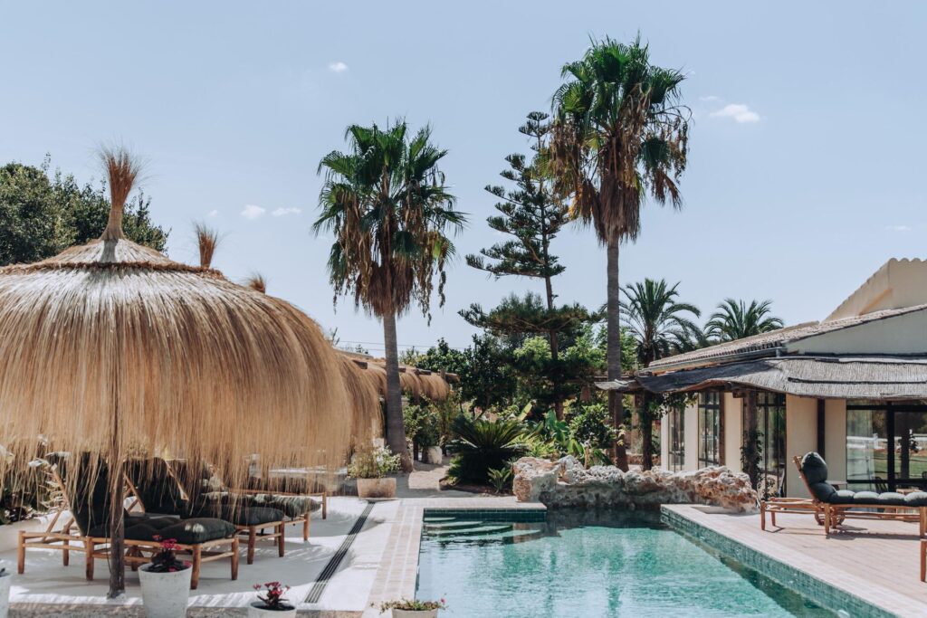 Finca Palmera pool framed by palms and thatched umbrellas.