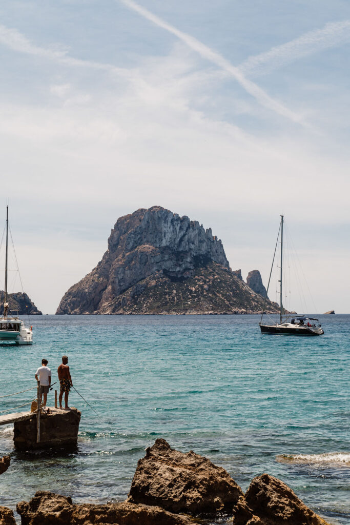 Firefly Villa in Es Cubells, Ibiza: view of Es Vedrà from Cala d’Hort, with boats on the turquoise water.