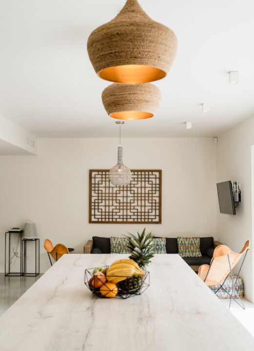 Dining area at Sa Brisa Villa in Santa Eulalia, Ibiza, with a fruit bowl on a marble table beneath woven pendant lights.