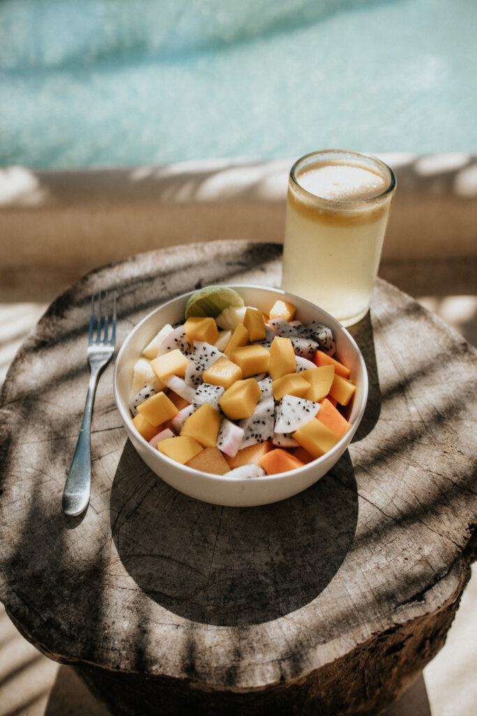 Bowl of fresh tropical fruit with a glass of juice beside a pool.