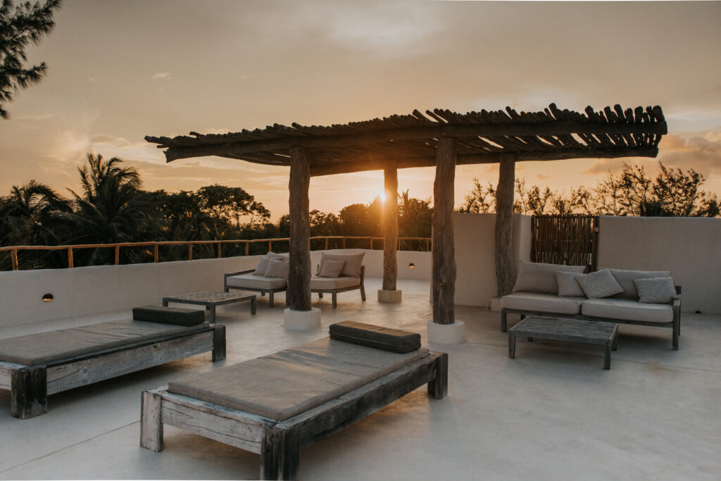 Outdoor lounge beneath a wooden pergola at sunset.