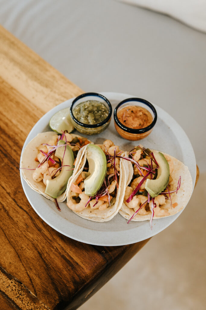 Shrimp tacos topped with avocado, served with lime and salsa.