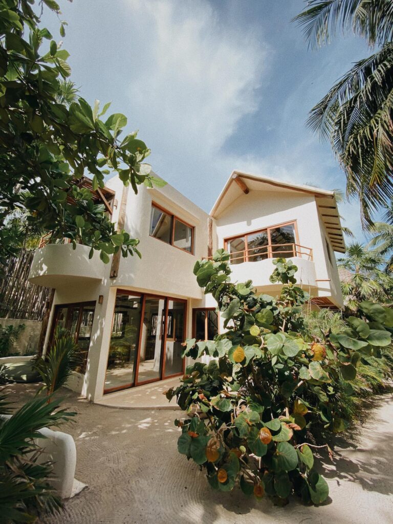 Low-angle view of a white, two-story villa framed by tropical leaves and palm trees.