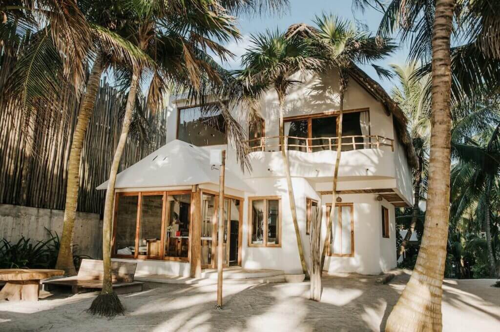 Sunlit view of the villa’s white exterior, wood-framed windows, and sandy courtyard.