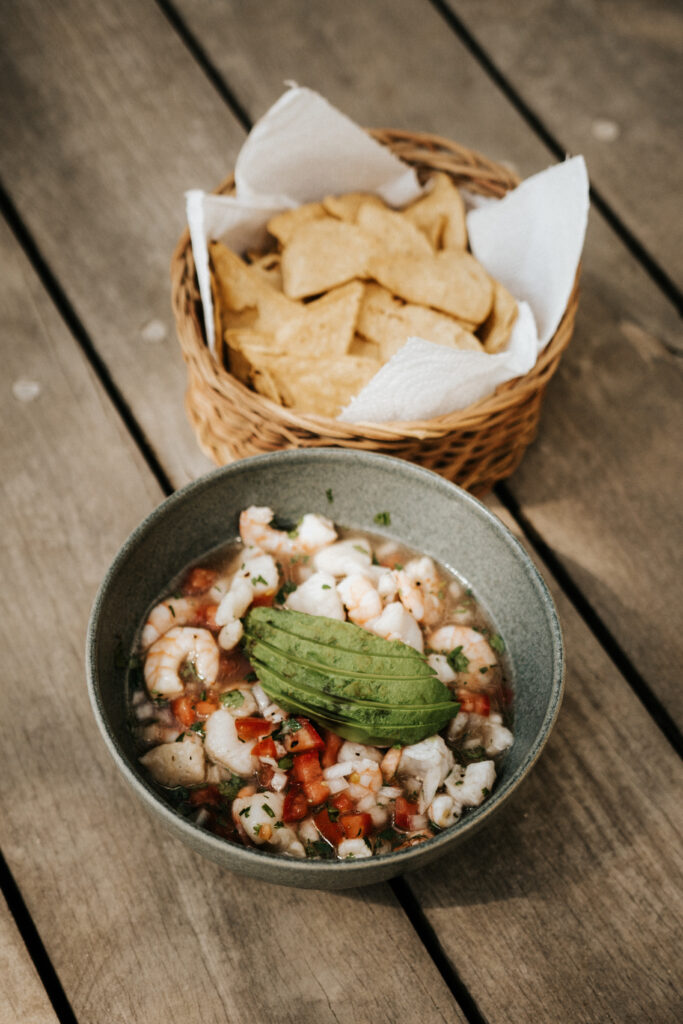 Bowl of shrimp and diced seafood with avocado, served with crackers in a woven basket.