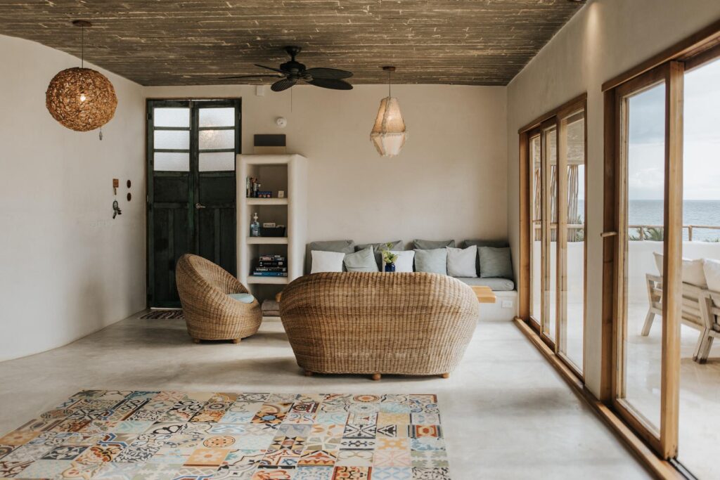 Wicker lounge chairs and a built-in sofa face glass doors opening to an ocean-view balcony.