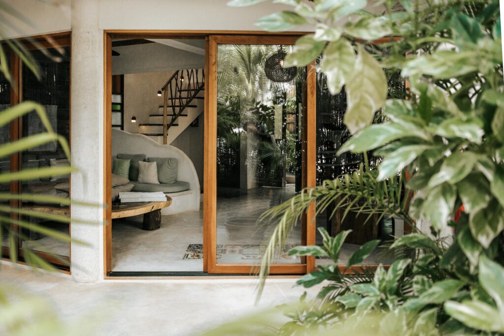 Open wood-framed glass doors reveal a built-in living room sofa and staircase inside the villa.