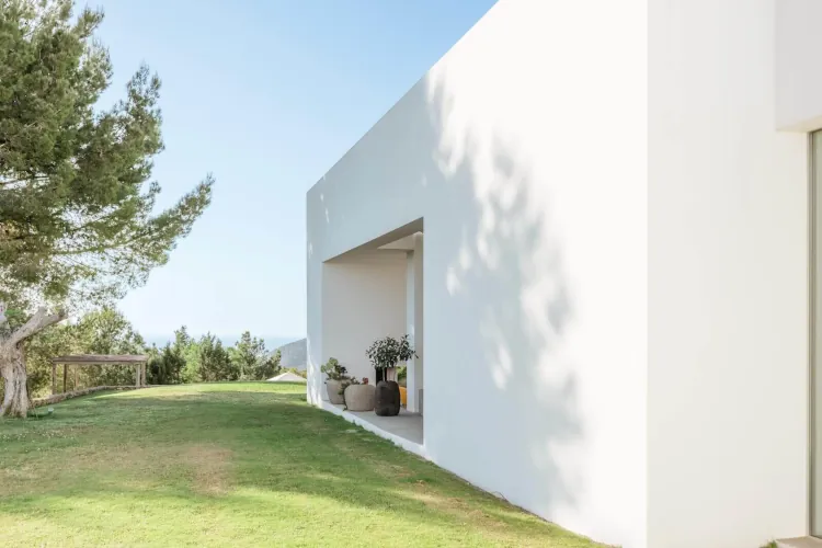 Modern minimalist white building with clean lines and an open archway. Surrounded by lush green grass and trees, conveying tranquility and simplicity.