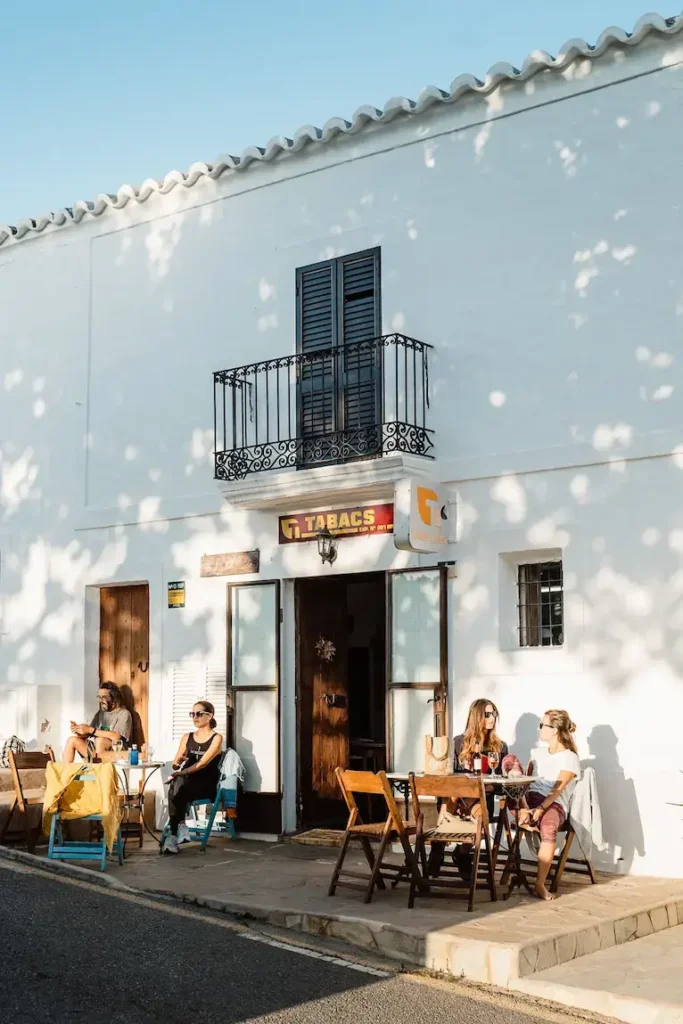Sunny street scene showing people sitting at tables outside a white building with a 