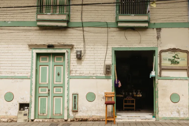 A weathered building facade features a pastel green door and a dark, open doorway with pottery inside. A wooden chair sits outside, evoking a rustic feel.