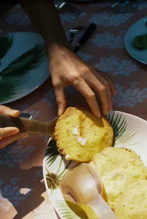 Hands serving fresh fried arepas on tropical patterned plate with green foliage background during outdoor meal