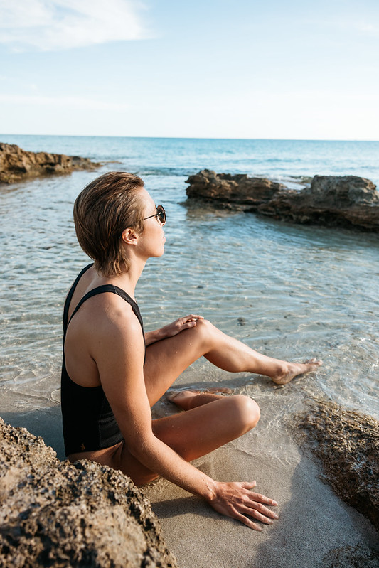 Woman sitting beside shallow Mediterranean water on a rocky coastline