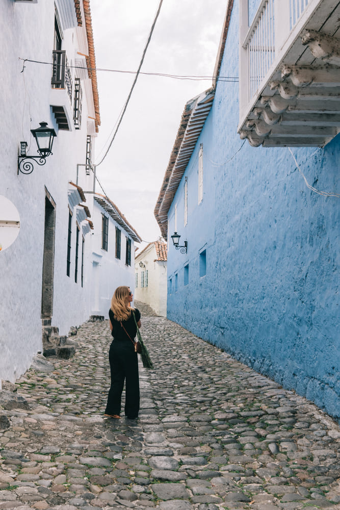 A traveler walking along a narrow cobblestone street lined with white and blue colonial buildings and traditional tiled roofs