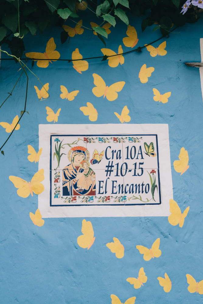 A vibrant blue wall decorated with yellow butterfly illustrations surrounding a hand-painted address sign for El Encanto