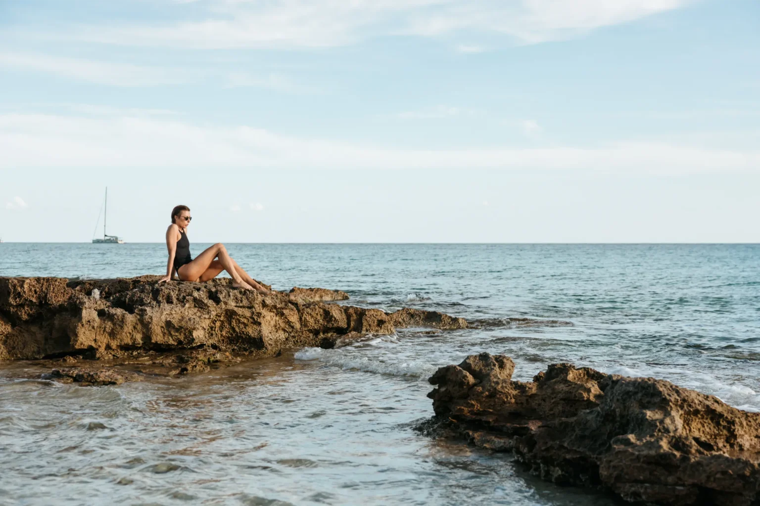 Woman sitting on rocky coastline overlooking the sea at Migjorn, Formentera