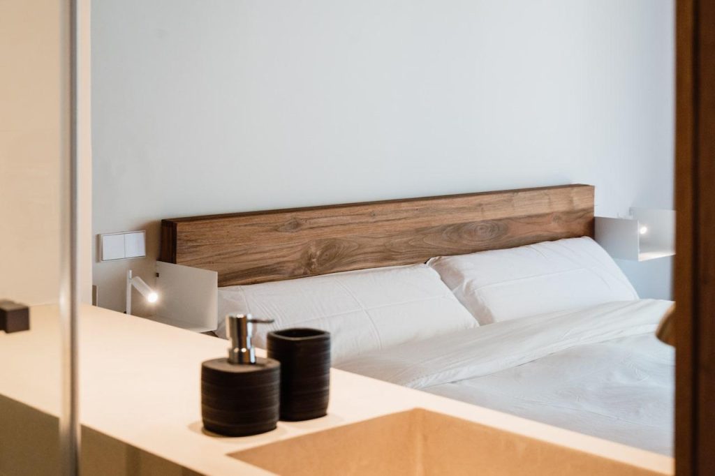 Bedroom at Can Beia Villa in Ibiza, with a white bed, wooden headboard, and bathroom vanity in the foreground.