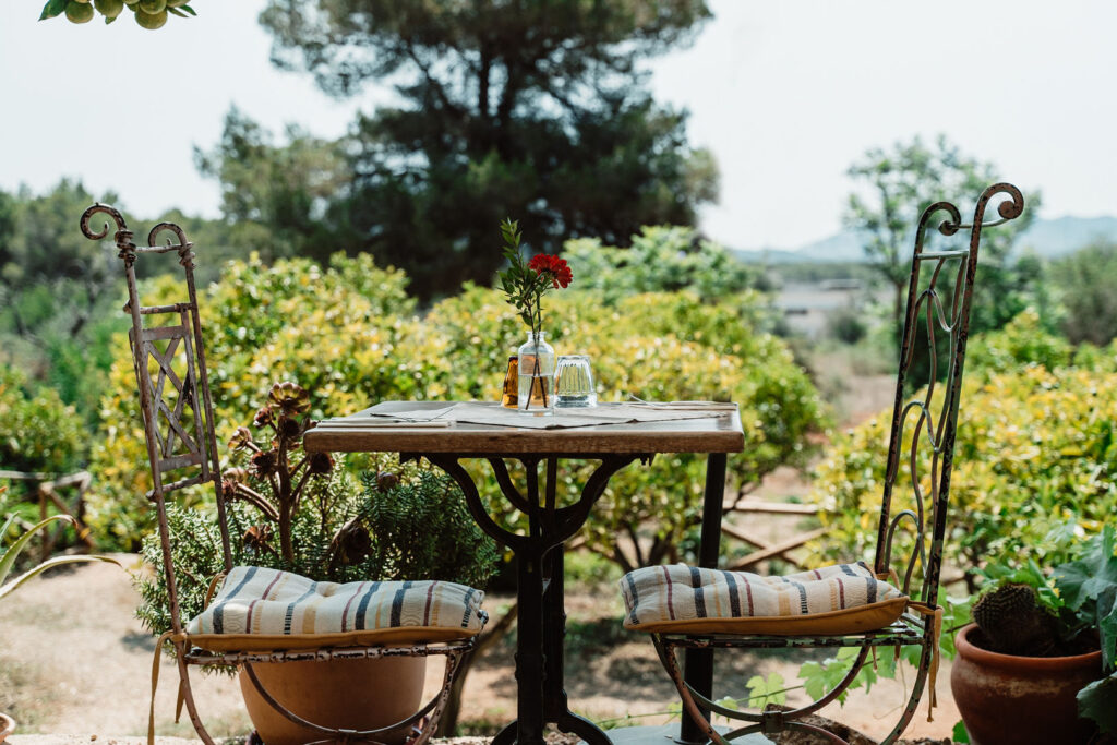 Can Beia Villa, Ibiza: garden dining at La Paloma, with a flower-topped table and wrought-iron chairs.