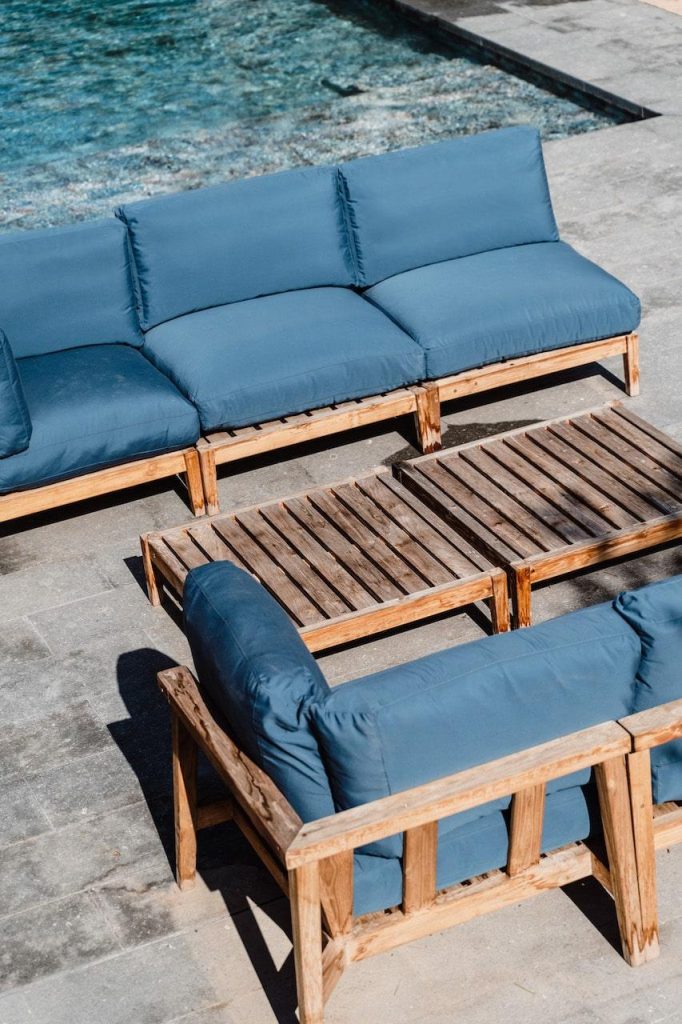 Poolside lounge at Can Beia Villa in Ibiza, with blue-cushioned wooden sofas and low tables beside the water.
