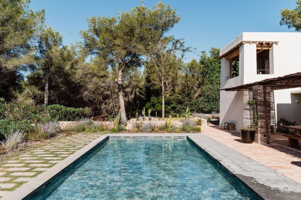 Swimming pool at Can Beia Villa in Ibiza, bordered by a stone patio and landscaped garden.