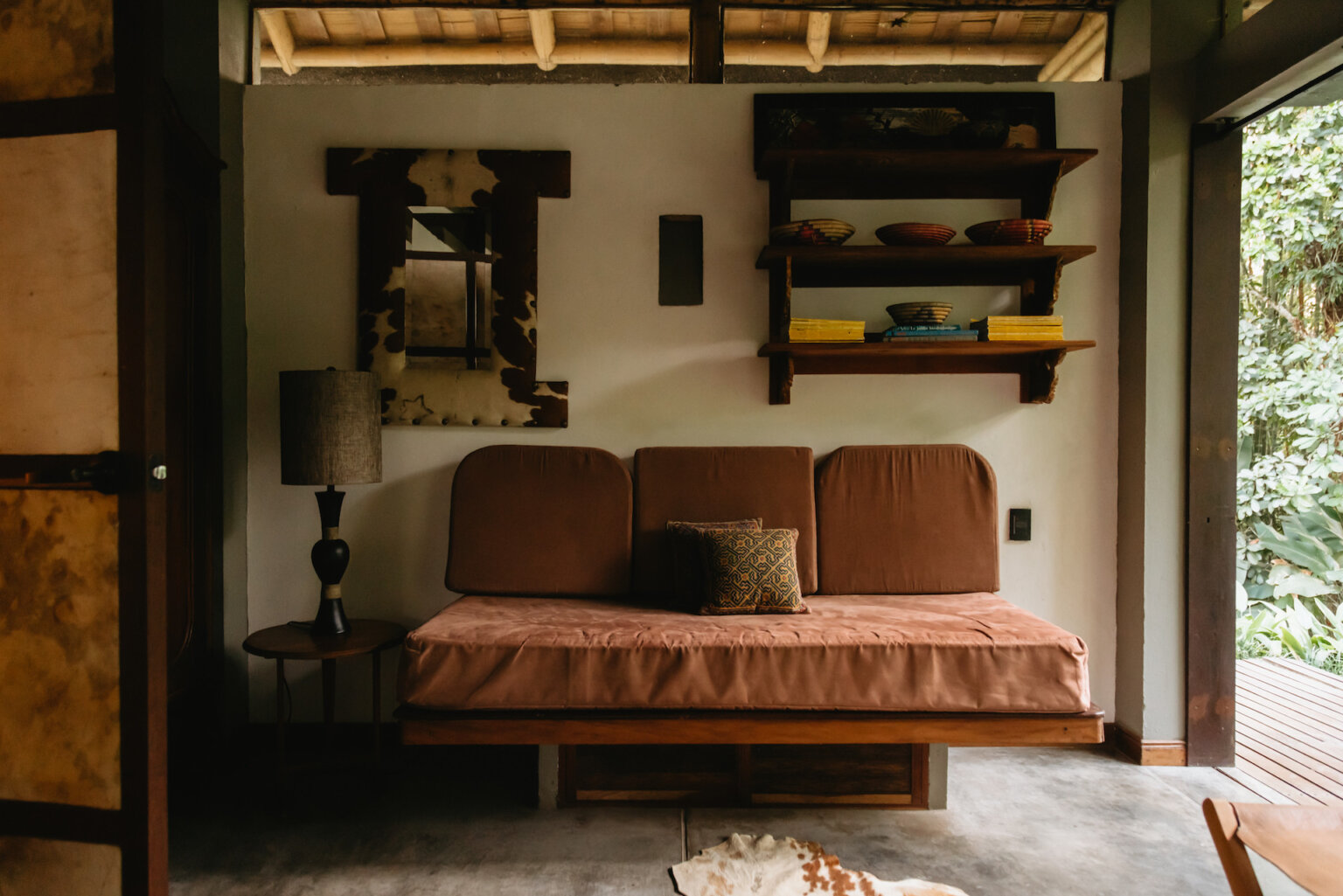 Rustic cabin interior with a brown daybed, cowhide-framed mirror, and wooden shelves.