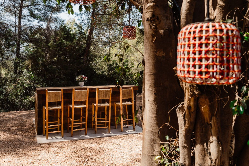 Garden bar table beneath trees at Villa Lunara, with woven stools and hanging lanterns.