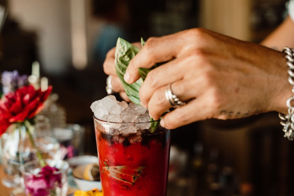 Bartender garnishes a red cocktail with fresh basil at La Paloma, Ibiza.