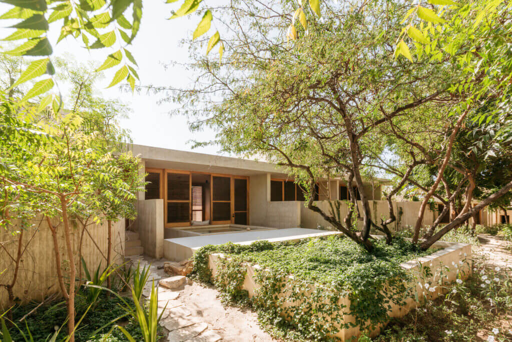 Low modern villa surrounded by trees, with a pool and garden in front.