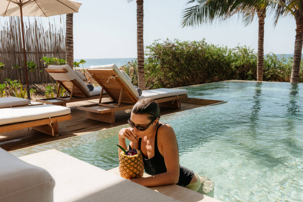 Guest in the pool drinks from a pineapple beside the ocean-view deck.