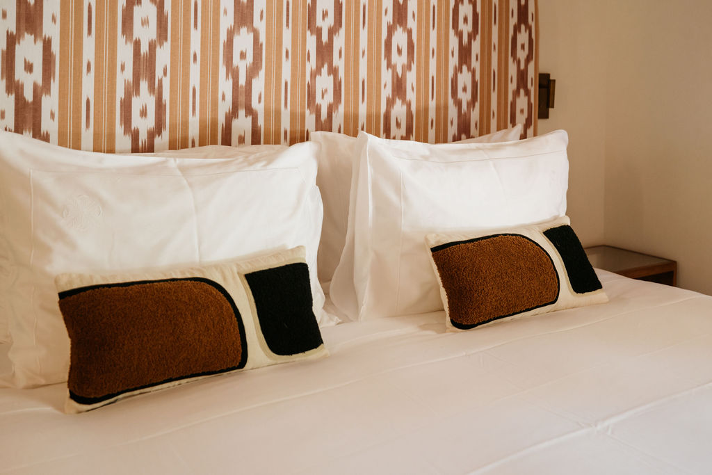 White bed linens and rust-and-black accent pillows against a patterned bedroom wall.