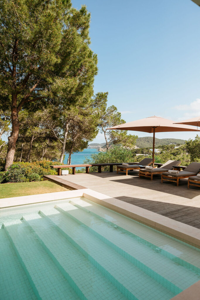 Villa Arcana’s shallow swimming pool and sun terrace overlook the sea through pine trees.