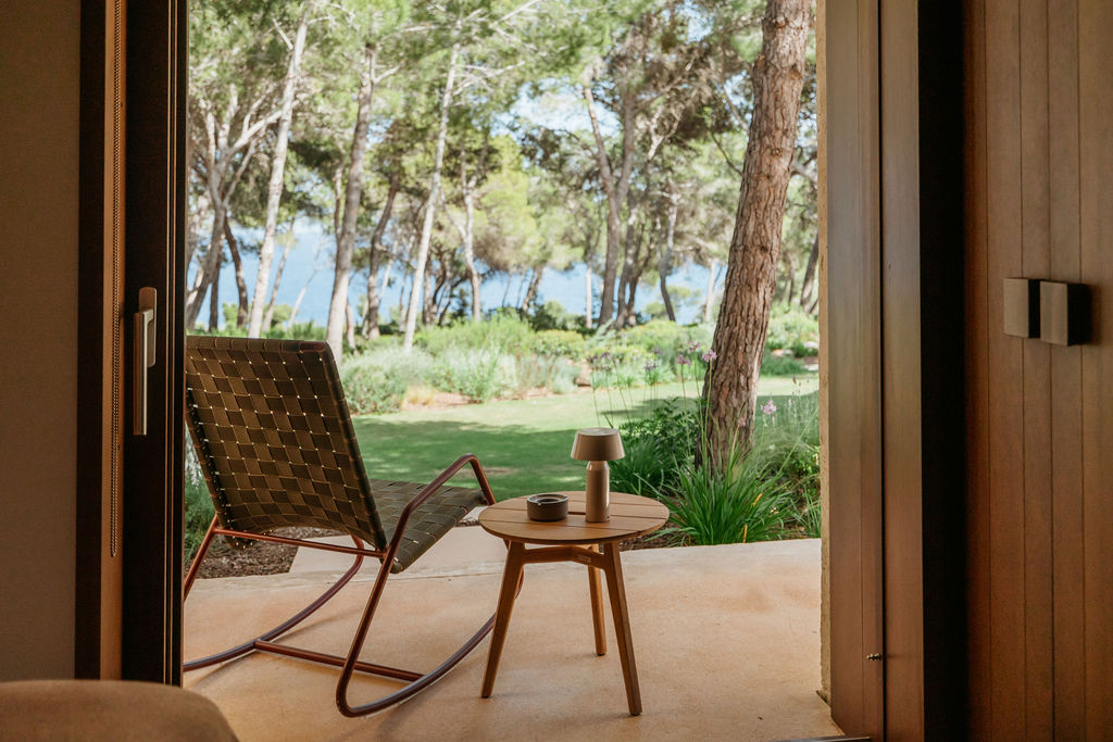 A lounge chair and small table on a shaded terrace overlooking the villa garden and sea.