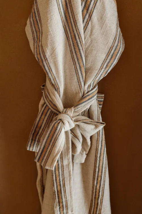 Beige and ochre striped linen robe tied with a knot belt, hanging against warm brown wall, boho spa or boutique hotel texture and detail