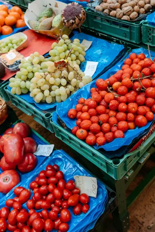 A vibrant market stall features clusters of green grapes, ripe red cherry tomatoes, and walnuts. Bright displays evoke freshness and abundance.