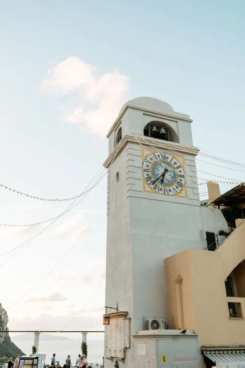 A tall stone tower with a large, colorful clock face and Roman numerals under a clear blue sky, creating a serene and timeless atmosphere.