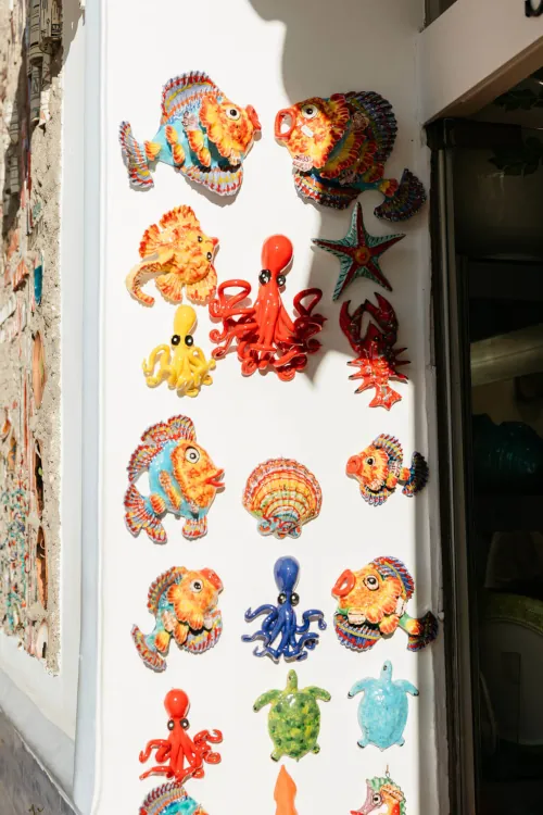 Colorful ceramic sea creatures, including fish, octopuses, turtles, and a starfish, decorate a wall in bright sunlight, conveying a playful, artistic vibe.