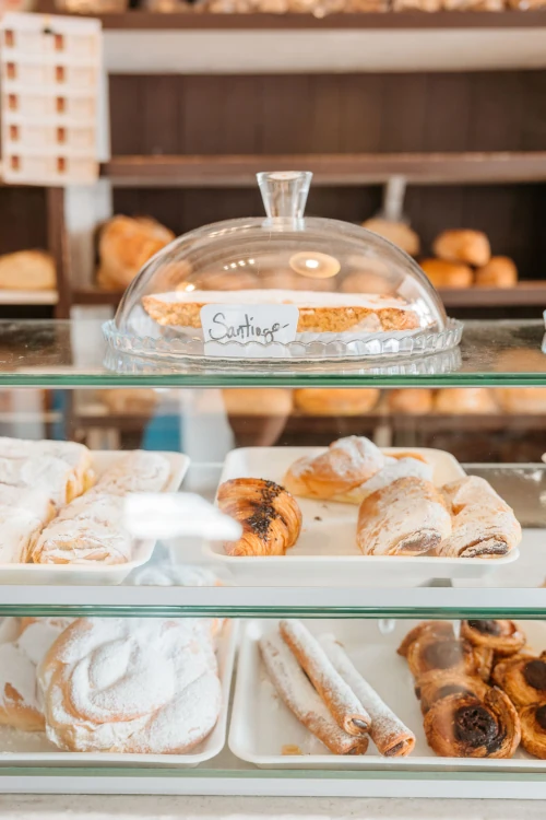 Bakery display case with assorted pastries, including sugar-dusted rolls and pastries under a glass dome labeled 