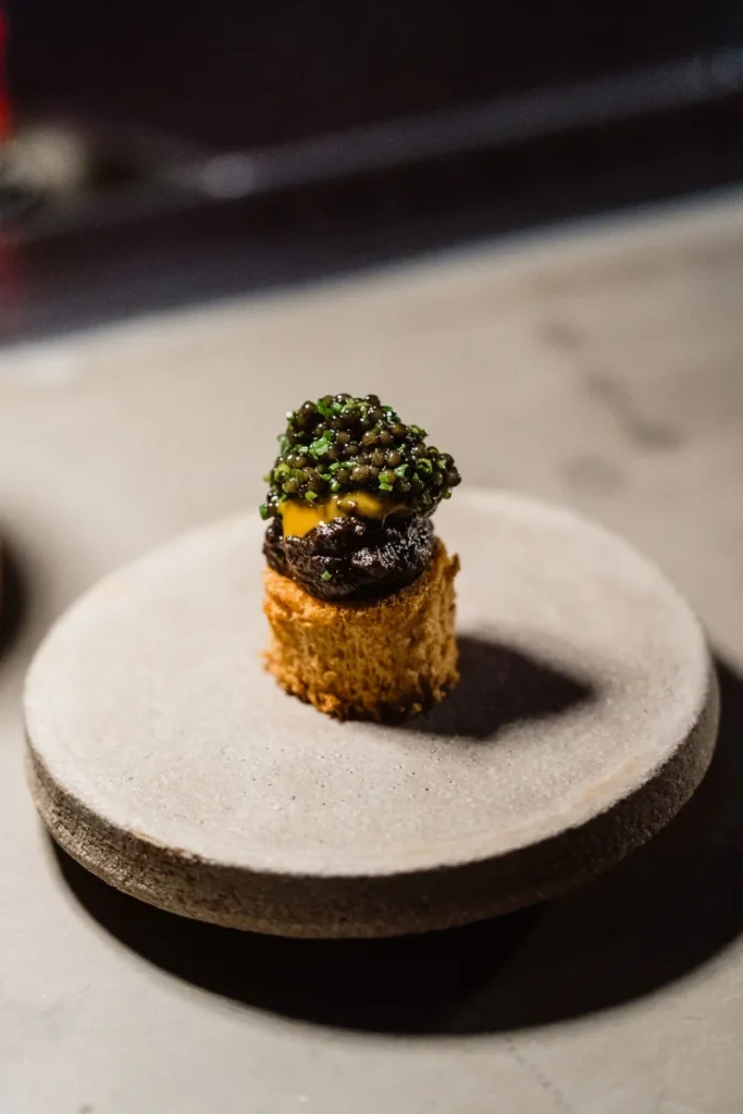 A delicate appetizer sits elegantly on a round stone plate. It features caviar atop a golden, textured base, exuding sophistication and culinary artistry.