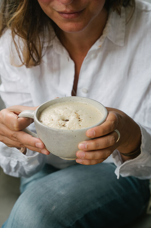 Close-up of a person in a white linen shirt holding a large ceramic mug of frothy Colombian coffee at a cafe in Barichara.
