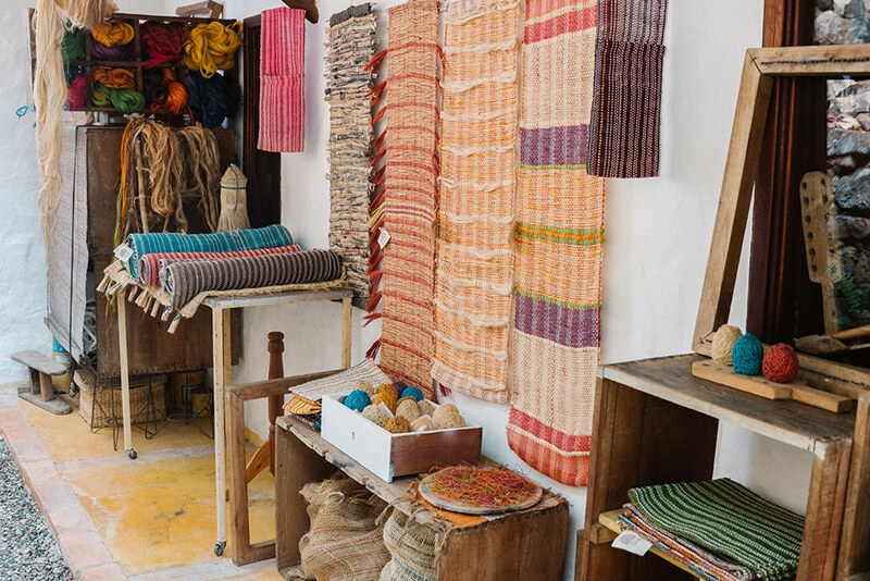 An artisan workshop in Barichara displaying rolls of handwoven rugs, spools of colorful yarn, and raw natural fibers used for luxury villa decor.