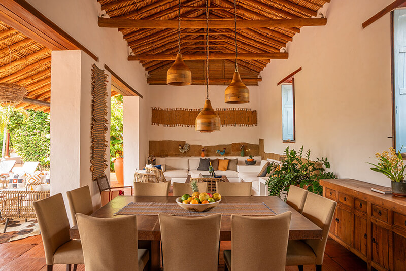 Spacious open-plan dining and living area in a luxury villa in Barichara, featuring a large wooden table, white sectional sofa, and traditional high thatched ceilings.