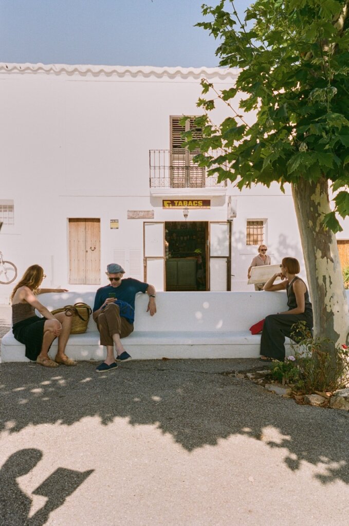 Visitors relax on a shaded bench outside a village shop in Ibiza.