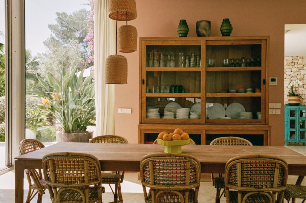 Wooden dining table with fresh fruit and woven chairs in the bright dining room at luxury villa Can Paloma, Ibiza.